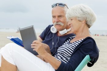 happy senior couple with tablet pc sitting on the beach