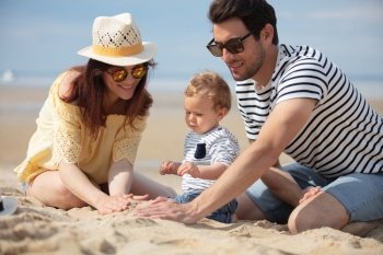 two parents and their toddler playing together in the sand