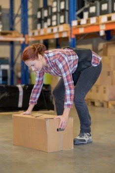 warehouse manager picking up cardboard box in a large warehouse