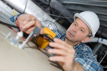 mature electrician inspecting building electrical system in ceiling