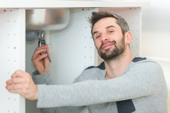 male plumber installing kitchen sink using wrench