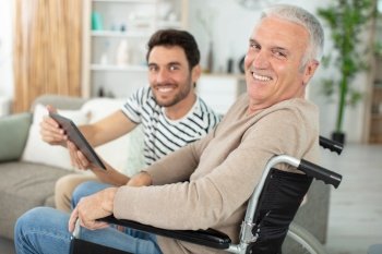 happy father in wheelchair and son using tablet