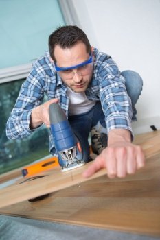 man using jigsaw to cut through floorboard