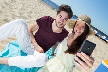 gorgeous young couple sitting at the beach and doing selfie