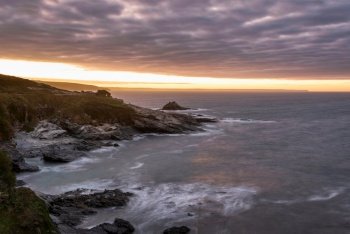 Moody landscape sunrise image at Prussia Cove in Cornwall England with atmospheric sky and ocean