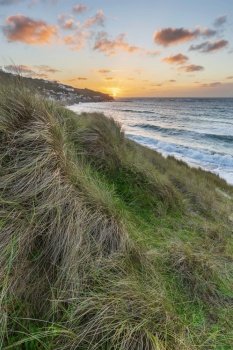 Beautiful landscape of Sennen Cove in Cornwall during sunset viewed from grassy sand dunes with moody sky and long exposure sea motion