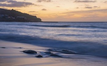 Beautiful landscape of Sennen Cove in Cornwall during sunset with moody sky and long exposure sea motion