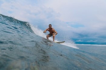 Male surfer on a blue wave at Bali island