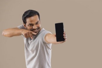 Happy young man pointing his finger at the smartphone holding in his other hand