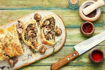 Closed homemade mushroom pie. Sliced savoury mushroom champignons pie on old kitchen board. Seasonal traditional mushroom pie.