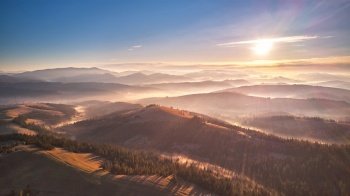 Mountain autumn Sunrise. Majestic Morning fog, Beautiful tonal perspective. Fall sunny Landscape, misty forest on hills. Majestic aerial scenery of valley, Carpathian range Ukraine.