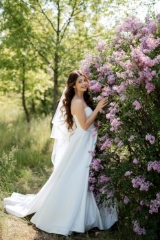 young girl bride in a white dress in a spring forest in lilac bushes on a wedding day