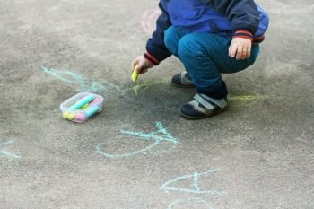 The child draws with chalk on the pavement. Children’s creativity of the child in the warm season in the fresh air.