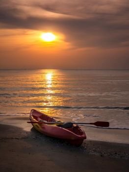 Sunrise with orange morning sky over sea with kayak boat on beach, Thailand