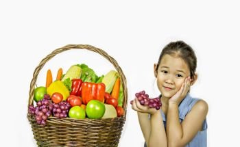 Smiling asian little girl  with fruits and vegetables in basket over white background. little girl  with basket