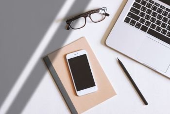 Flat lay photo of office desk with laptop, smartphone, eyeglasses and notebook with copy space background