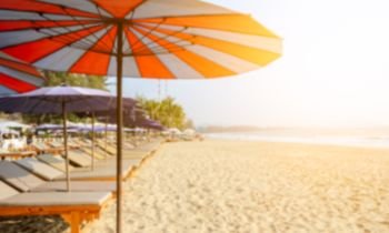 Blurred row of sun beds and colorful umbrellas on tropical sandy beach with sunlight