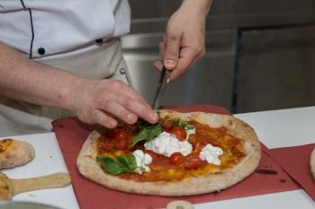 Pizza Maker who Prepares a Delicious Pizza with Cheese,  Cherry Tomatoes and Basil.. Pizza Maker who Prepares a Delicious Pizza with Cheese,  Cherry Tomatoes and Basil