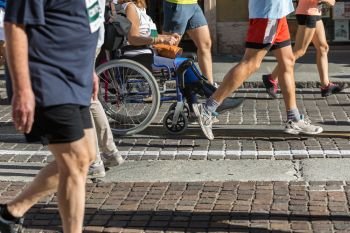 Woman with an injured Leg in a Wheelchair during Marathon Helped by Runners.. Woman with an injured Leg in a Wheelchair during Marathon Helped by Runners