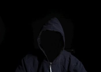 Anonymous criminal man in hood isolated on black background. Anonymous criminal man in hood