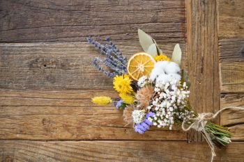 Still life of bouquet of dried flowers with orange segment on wooden background