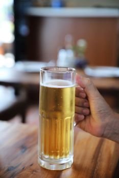 beer in tall glass on wood background with man hand