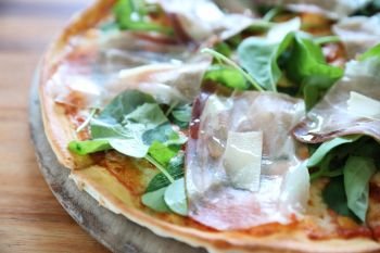 Pizza with parma ham salad rocket on tomato sauce with wood table background