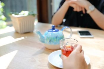 Woman hand with tea and smartphone talking business in coffee shop