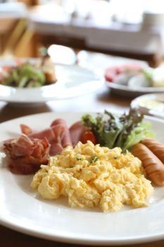 Breakfast scrambled egg with bacon sausage and salad on wood background