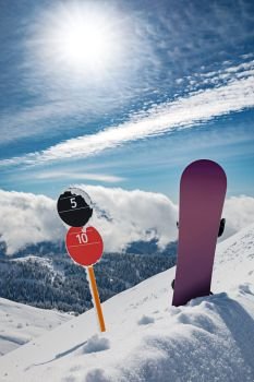 Slope number signs and snowboard standing upright on the edge of ski slope in snow. Sunny winter day at mountains 