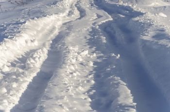 Road covered with snow. Tire tracks in deep snow. Sunny winter day.
