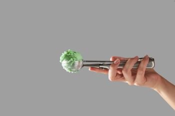 A female hand holds a metal scoop with green fruit ice cream on a gray background with space for text. Cold summer dessert.. A woman’s hand holds a scoop with homemade ice cream on a gray background with copy space.