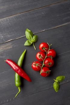 Ingredients for tomato sauce salsa. Fresh tomatoes, hot chili, basil on black wooden background. Top view. Italian food background with tomatoes, basil, and chili pepper on wooden background, flat lay