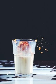 Delicious biscuit in a glass of milk and spilled milk on a black wooden background with copy space. Traditional Christmas treat for Santa - homemade oatmeal cookies.. Homemade peanut cake fall to a glass of milk with splash on a black wooden table.