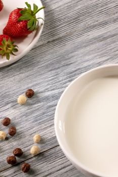 Chocolate and white grain balls with strawberries and of milk plate on a gray wooden table with copy space. Top view. Ripe strawberries, cereal balls and a plate of milk on a gray wooden table. Top view