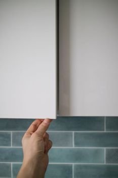 Opening kitchen cabinet door without handle with focus on male hand opening action. Modern furniture design without a door handle and locks. male hand opening kitchen cabinet door without handle