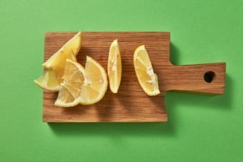 Healthy food concept. Top view of citrus fruit - slices of of yellow organic lemon on a wooden board on green.. Slices of juicy ripe natural yellow lemon on a wooden board on a green background. Top view.