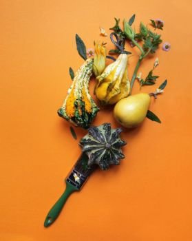 decorative pumpkins, green leaves, flowers, a pear and a brush on an orange background.The creative autumn composition flat lay. creative autumn composition of pumpkins