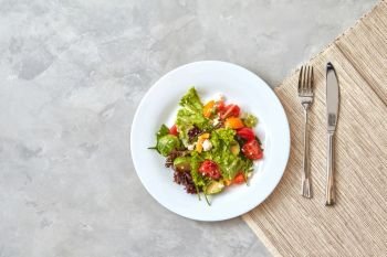 Portion Salad of fresh vegetables and cheese in a plate with a fork and knife on a gray background.step serving dishes, photo from Step by step recipe, Top view, flat lay.. Fresh vegetable salad in a plate with a fork and knife on a gray background,