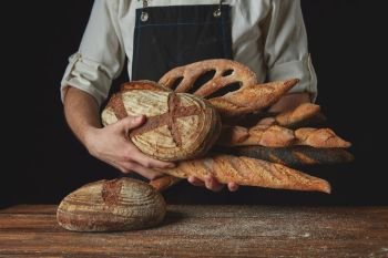 Men’s hands hold many different breadson a wooden table. Variety of bread hold men’s hands