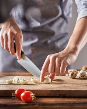 A woman in an apron slices quail eggs on a wooden board on an old wooden table. Step by Step diet salad. Cook woman in a gray apron cuts boiled quail eggs on a wooden board. Step by Step Cooking