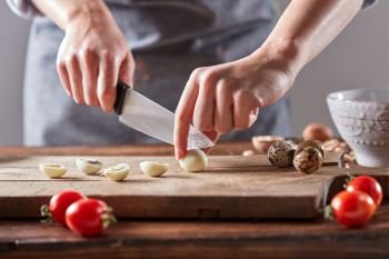 On a wooden table, the hands of a woman cut quail eggs on an old wooden board. Step by step salad preparation. Boiled quail eggs cut female hands on a wooden board on a table with tomatoes and spinach. Step by step preparation