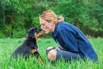 Young caucasian female dog owner  kisses rottweiler puppy on head in natural meadow