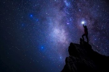 Silhouette of climber or backpacker. In his hand, he held the light up high above his head. Standing on rocky mountain peak and Milky Way Galaxy, success, winner, leader concept. High iso with Noise.. Leader on top.
