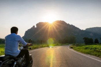 Biker man riding motorcycle on the road into the mountain with sunset and  ligth flare.. road into the mountain