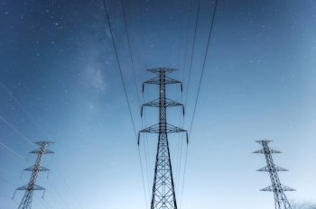 High voltage electricity pylon and transmission power line and a Parts of electrical equipment and high voltage power line insulators at night with milky way, Blue tone..  High voltage electricity pylon at night.
