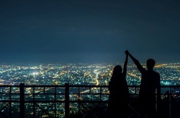 The silhouette of the couple holding hands to express their joy at the Chiang Mai city night view point.. Silhouette of couple in love.