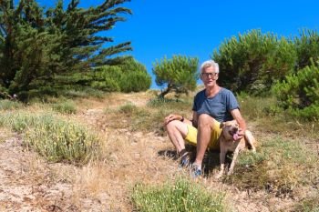 Ile de Re - Senior man sitting together with dog in the dunes 
