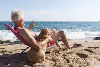 Senior man sun bathing with his dog at the beach under parasol with waves, sea and sand