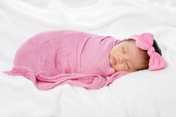 newborn baby sleep in pink cloth wrap blanket on a bed